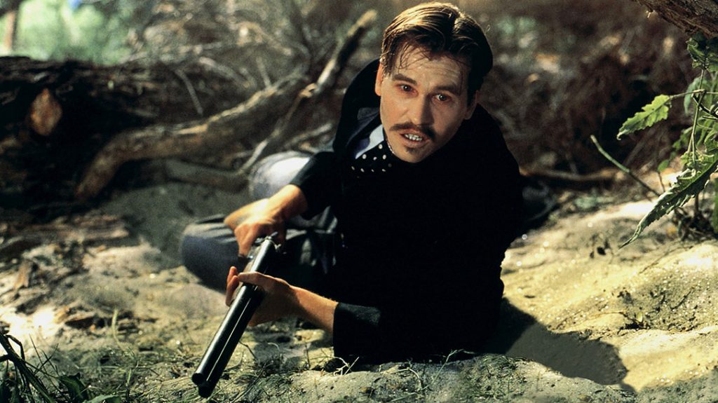 Val Kilmer wields a coach gun as Doc Holiday in arguably one of the best Wyatt Earp movies, Tombstone (1993).